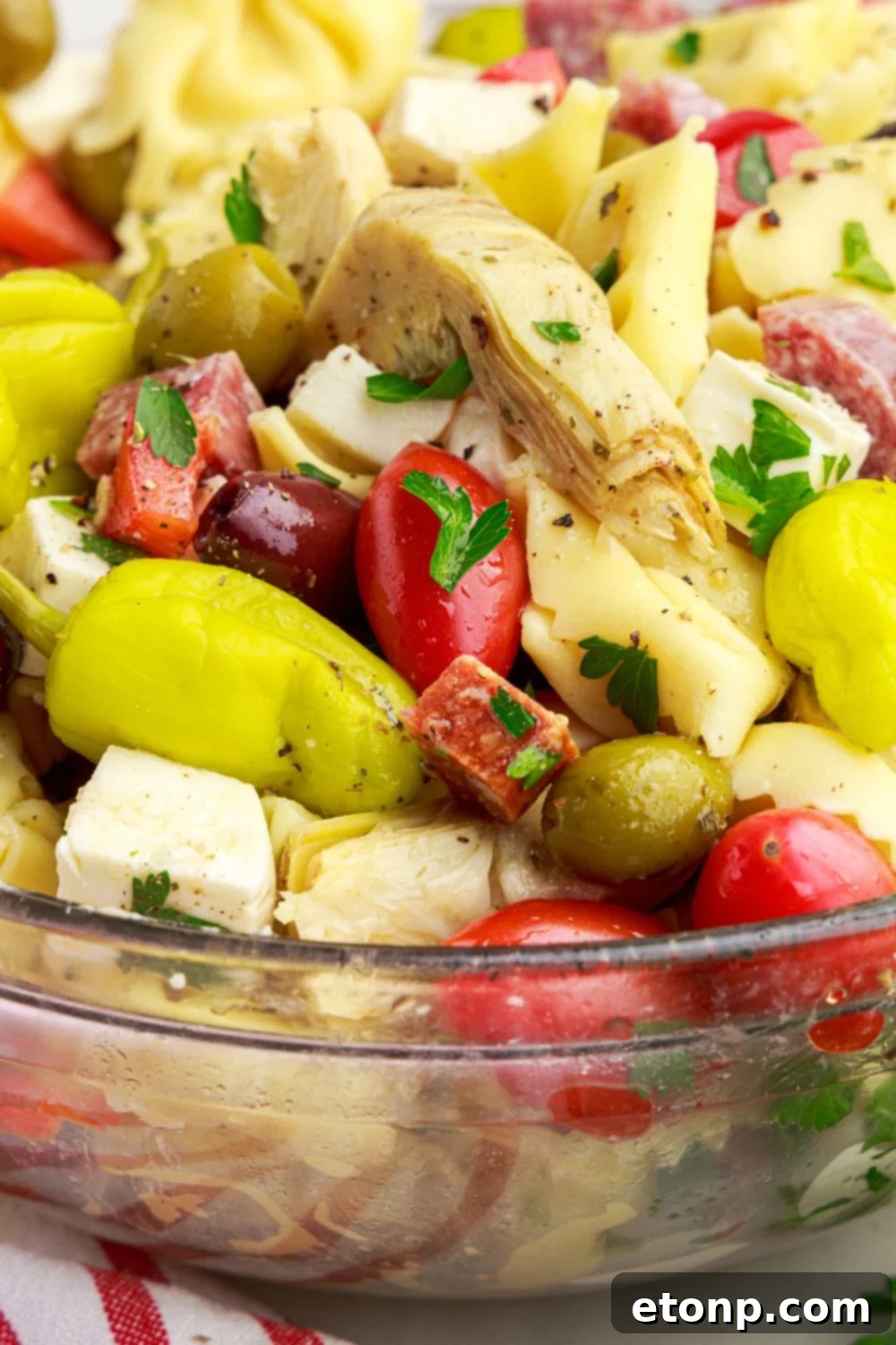 A close-up view of the Antipasto Tortellini Pasta Salad in a glass bowl, featuring artichokes, bell peppers, and other colorful components.
