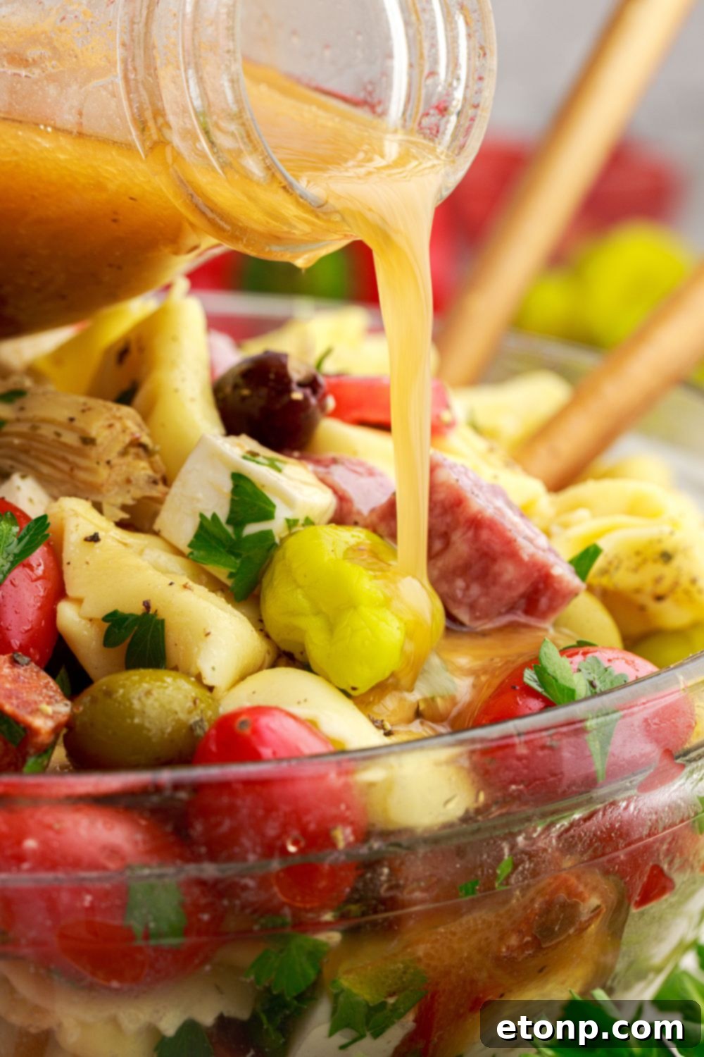Pouring Italian dressing into a bowl of Antipasto Tortellini Pasta Salad, enhancing its flavors.