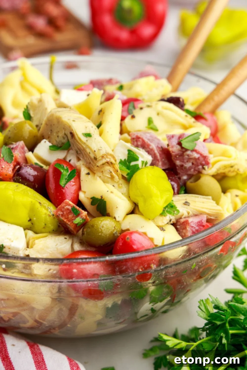 Antipasto Tortellini Pasta Salad in a glass bowl with serving spoons, highlighting its vibrant and inviting appearance.