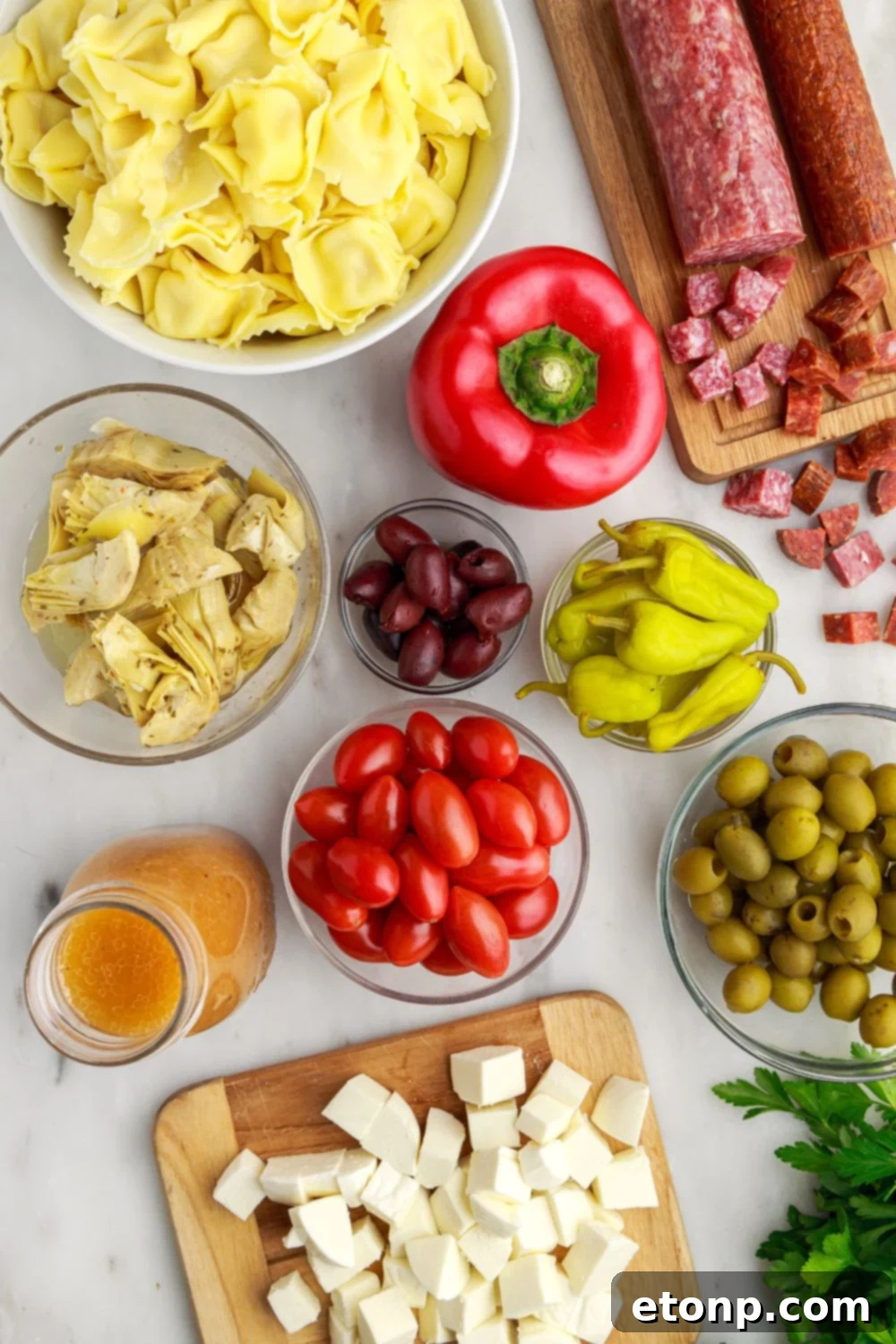 All the fresh ingredients for Antipasto Tortellini Pasta Salad, including tortellini, meats, cheeses, and vegetables, beautifully spread out on a table.