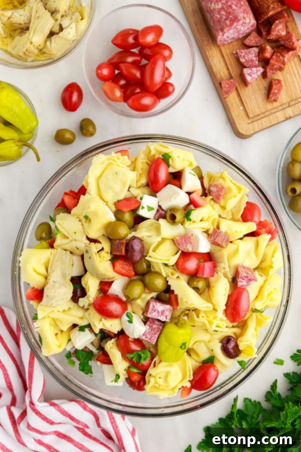 Antipasto Tortellini Pasta Salad being gently mixed in a large glass bowl, showing all the vibrant ingredients coming together.
