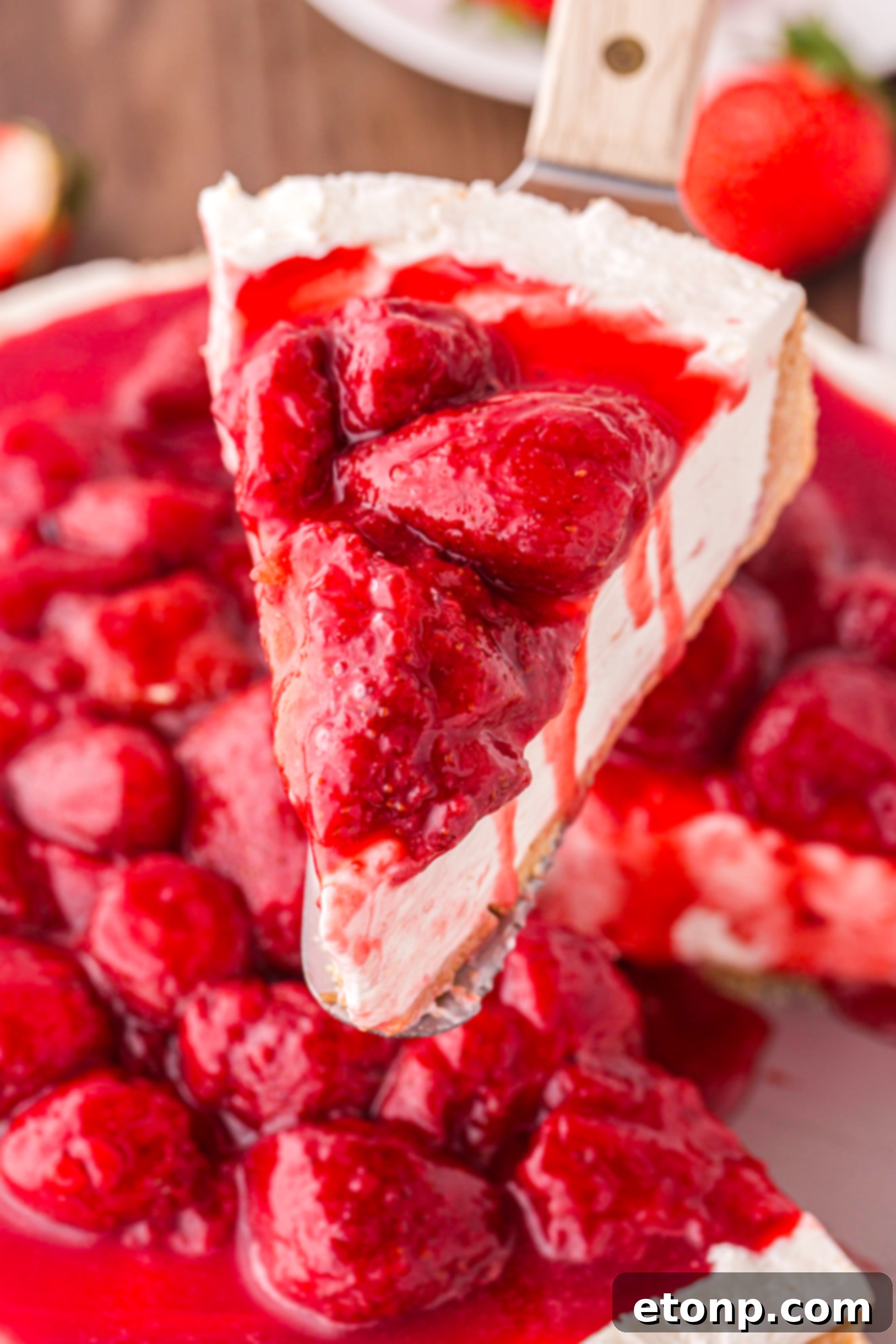 A perfectly sliced piece of No Bake Strawberry Cheesecake being lifted, revealing its creamy layers and rich strawberry topping.