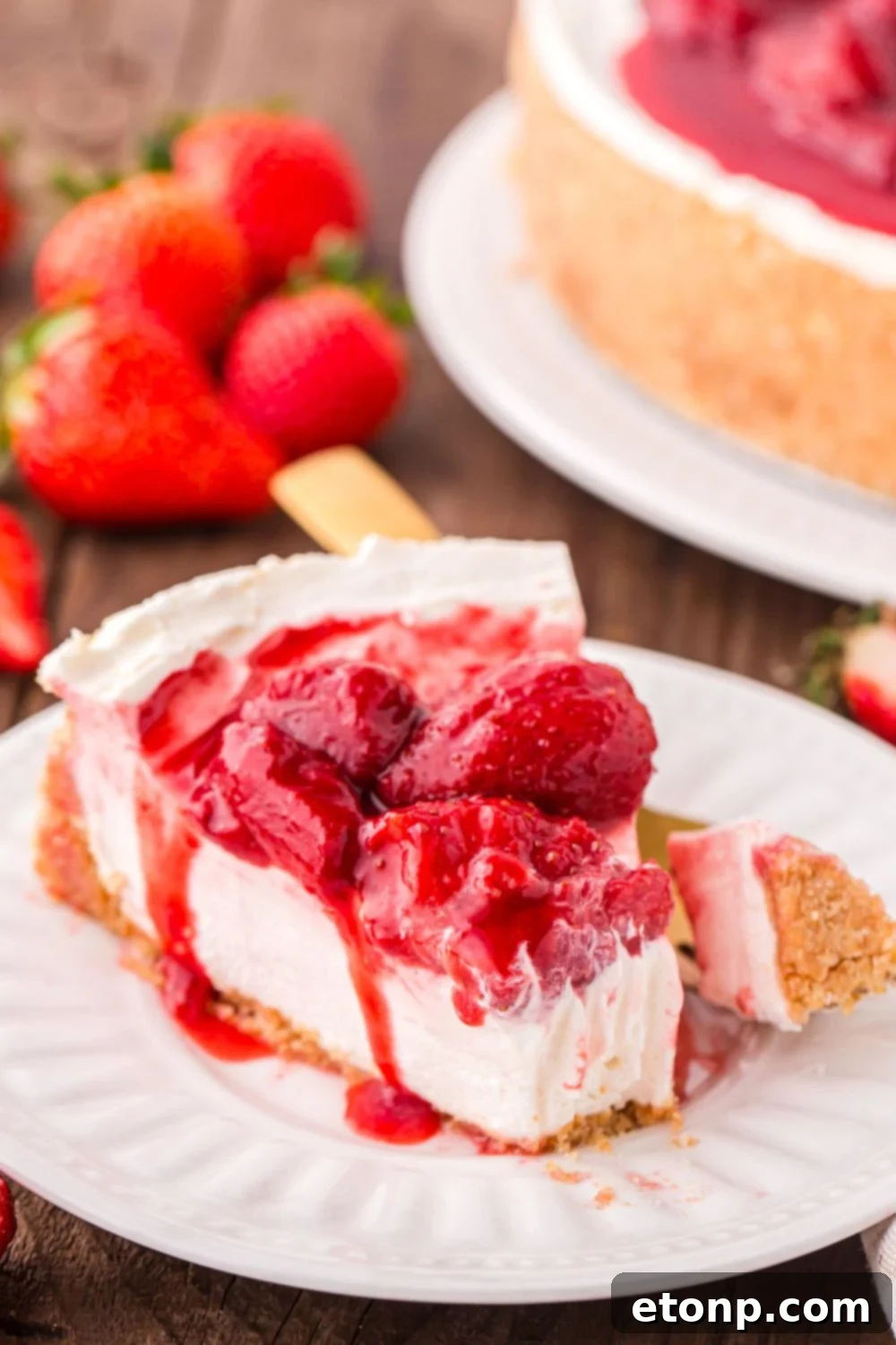 A delectable slice of No Bake Strawberry Cheesecake on a plate, with a fork holding a bite, and fresh strawberries artfully arranged in the background.