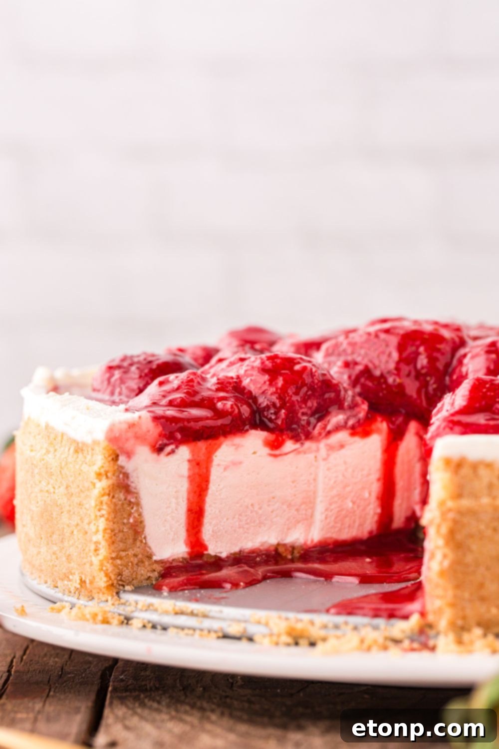 A beautiful top-down view of a strawberry cheesecake on a platter, with several slices already taken, revealing the generous thickness of the cheesecake layers.