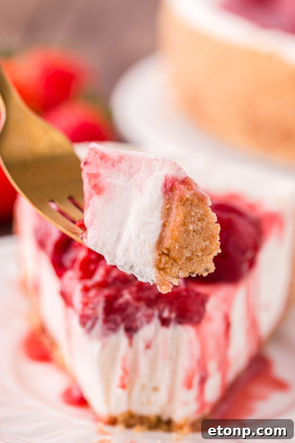 A slice of No Bake Strawberry Cheesecake on a plate, with a fork holding a bite, showcasing its creamy texture and fresh strawberry topping.