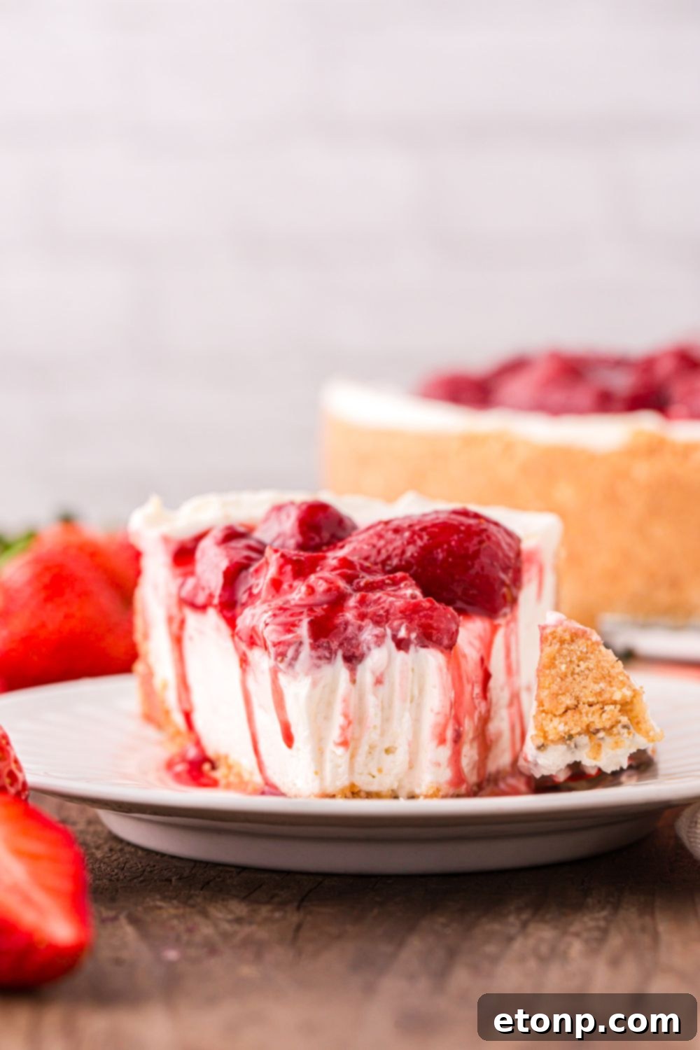 A delectable No Bake Strawberry Cheesecake on a plate, with a perfect wedge cut out, and the remainder of the cheesecake beautifully displayed on the table.