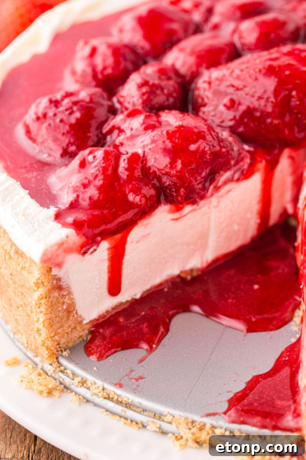 A captivating view of the strawberry cheesecake on a table, with luscious strawberry sauce gently dripping down its sides, highlighting its tempting appeal.