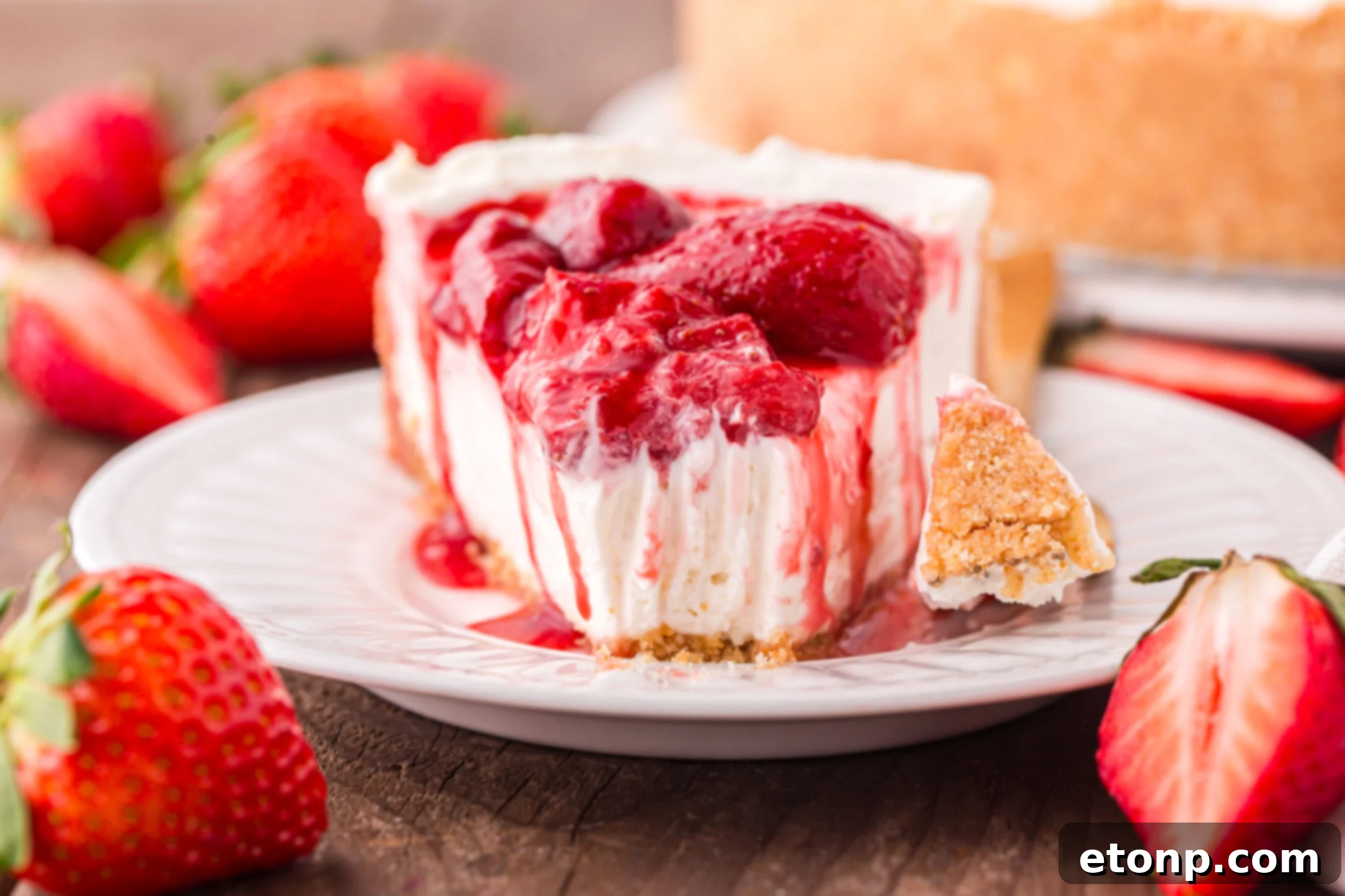 A close-up view of the No Bake Strawberry Cheesecake on a white plate, generously topped with plump, juicy strawberries, with a tempting bite missing.