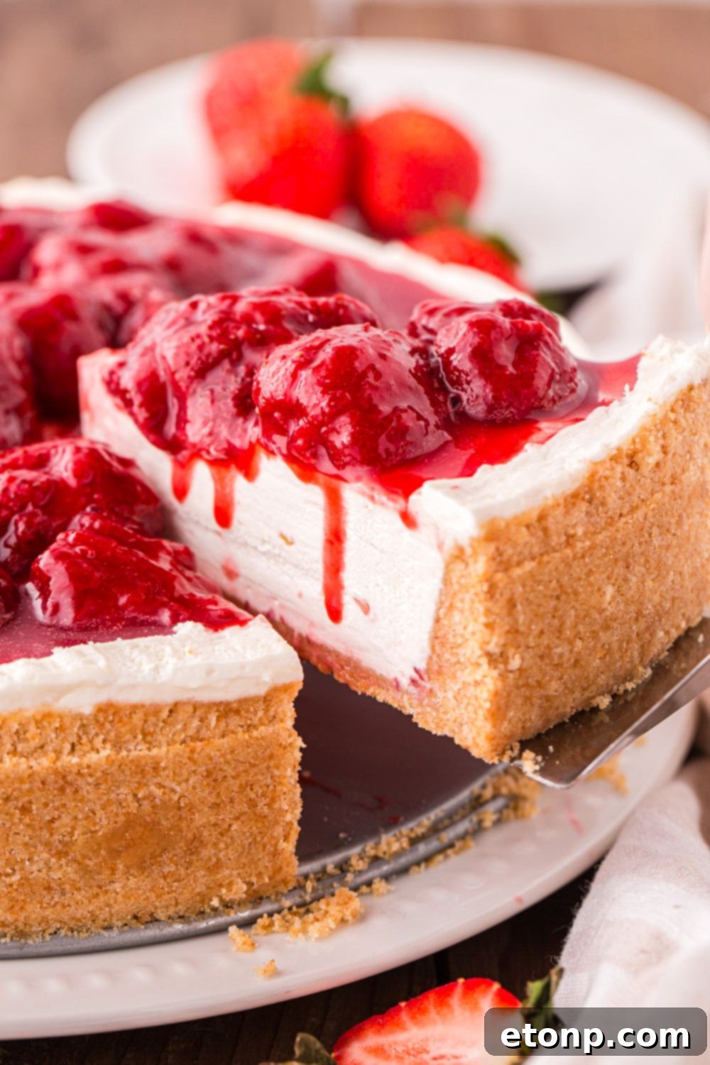 A slice of No Bake Strawberry Cheesecake being gracefully lifted from the pan, highlighting its vibrant layers and inviting appeal.