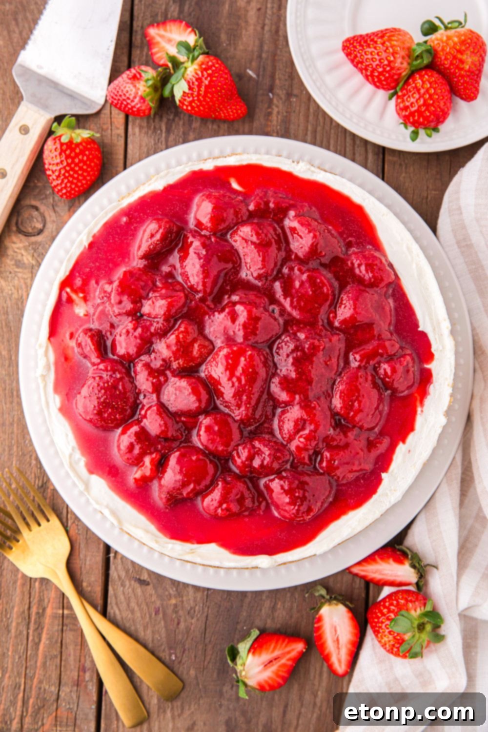 A stunning No Bake Strawberry Cheesecake, garnished with fresh strawberries, elegantly arranged on a table with plates and forks, ready to be served.