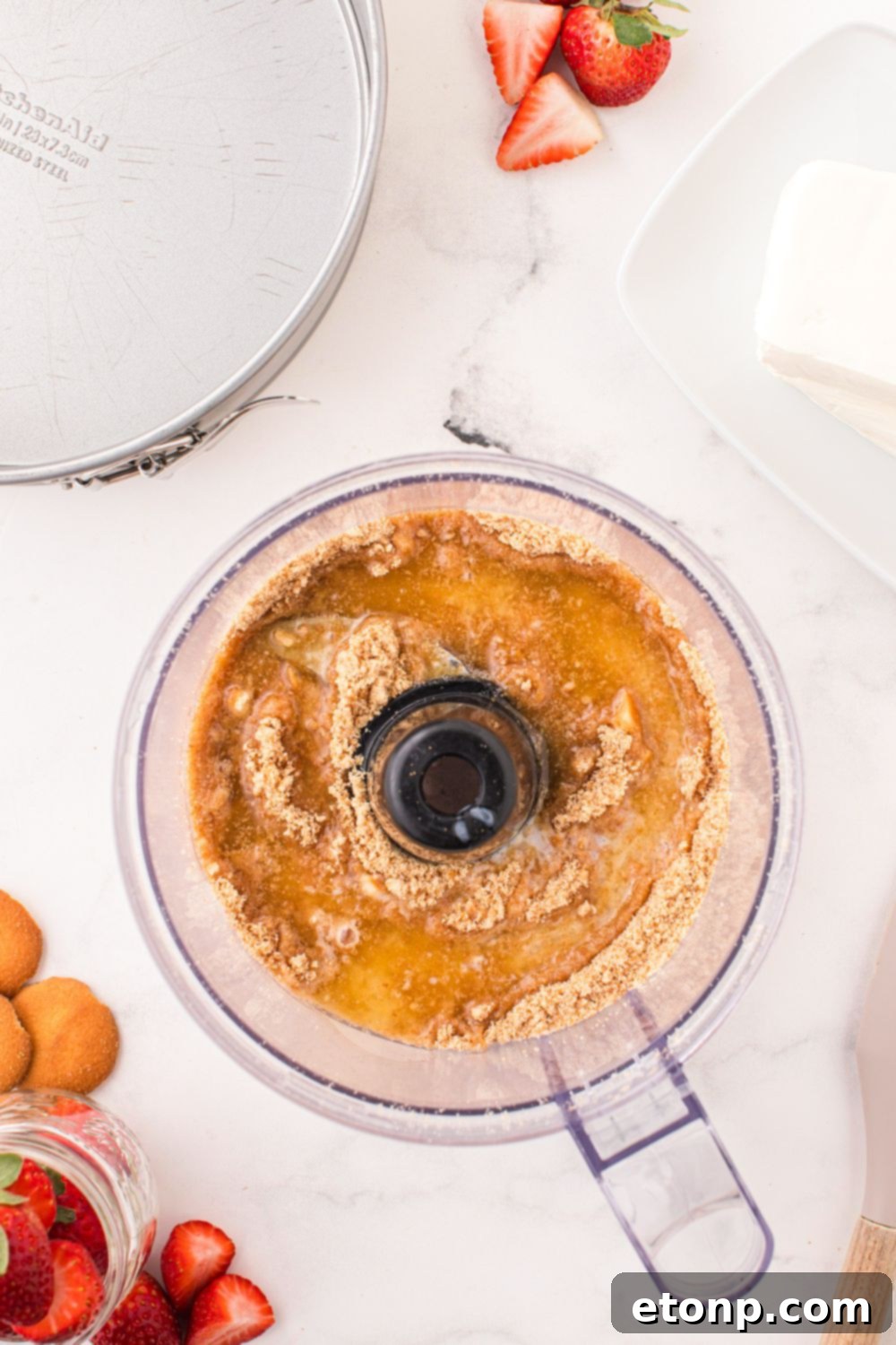 Crushed vanilla wafers and melted butter being combined in a food processor, forming the base for the cheesecake crust.