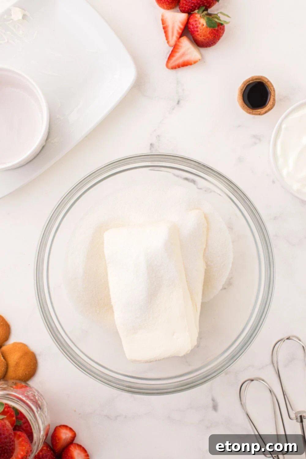 Cream cheese and granulated sugar being creamed together in a glass bowl, creating a smooth and fluffy base for the cheesecake filling.