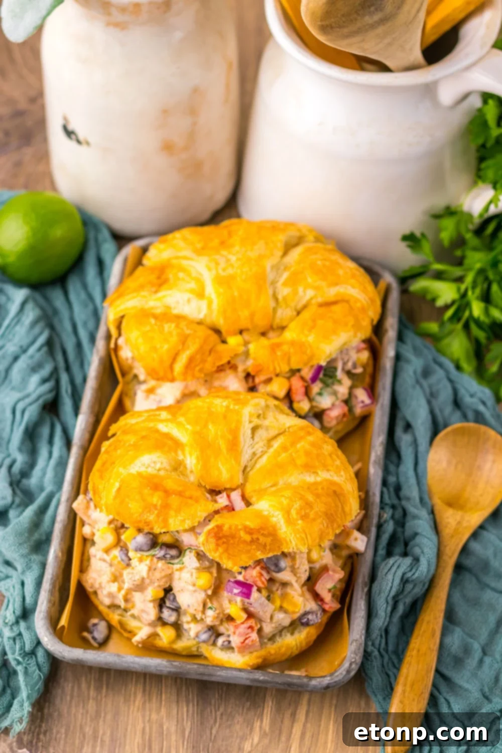 Creamy Taco Chicken Salad sandwiches on a table with a rustic towel, lime, cilantro, and various other decorative elements.