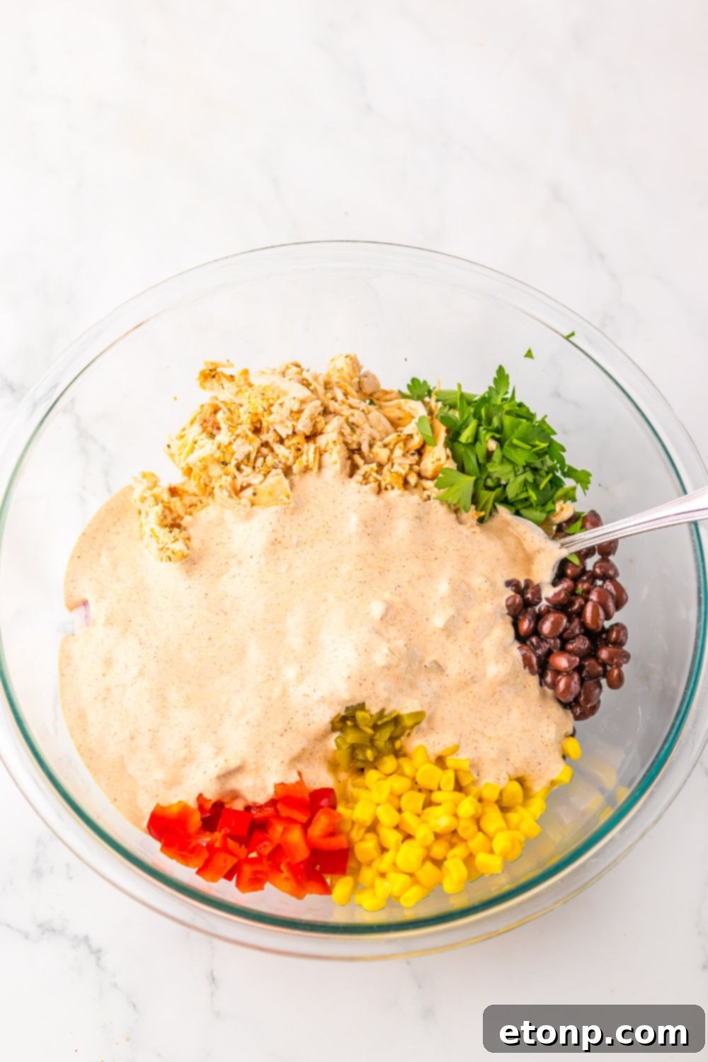 Creamy Taco Chicken Salad ingredients in a bowl, with the prepared dressing being poured over them.