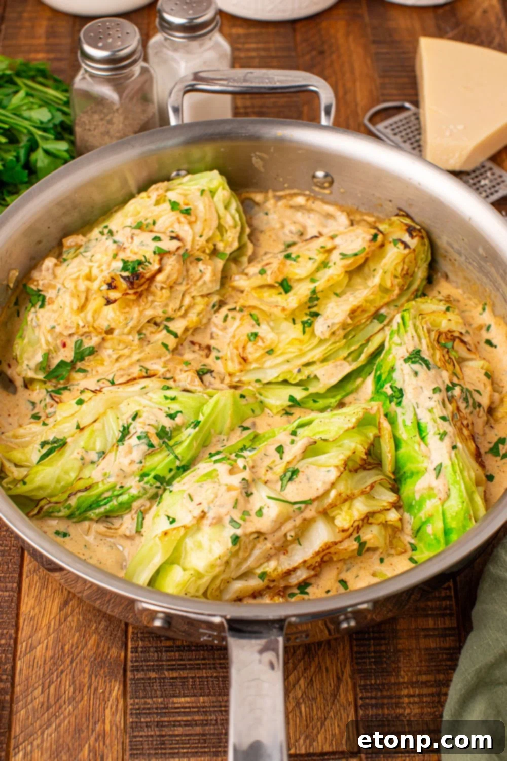 Creamy Garlic Parmesan Cabbage in a skillet sitting on table with a wedge of parmesan to side, salt and pepper, etc
