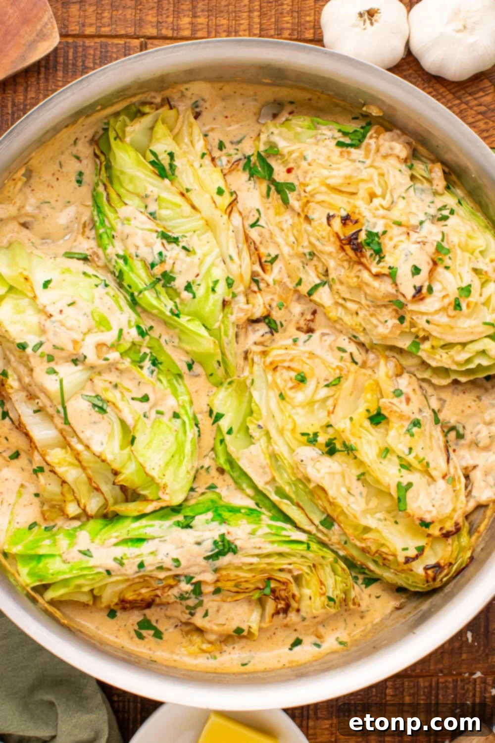 Creamy Garlic Parmesan Cabbage in a skillet on table with garlic bulbs to side 
