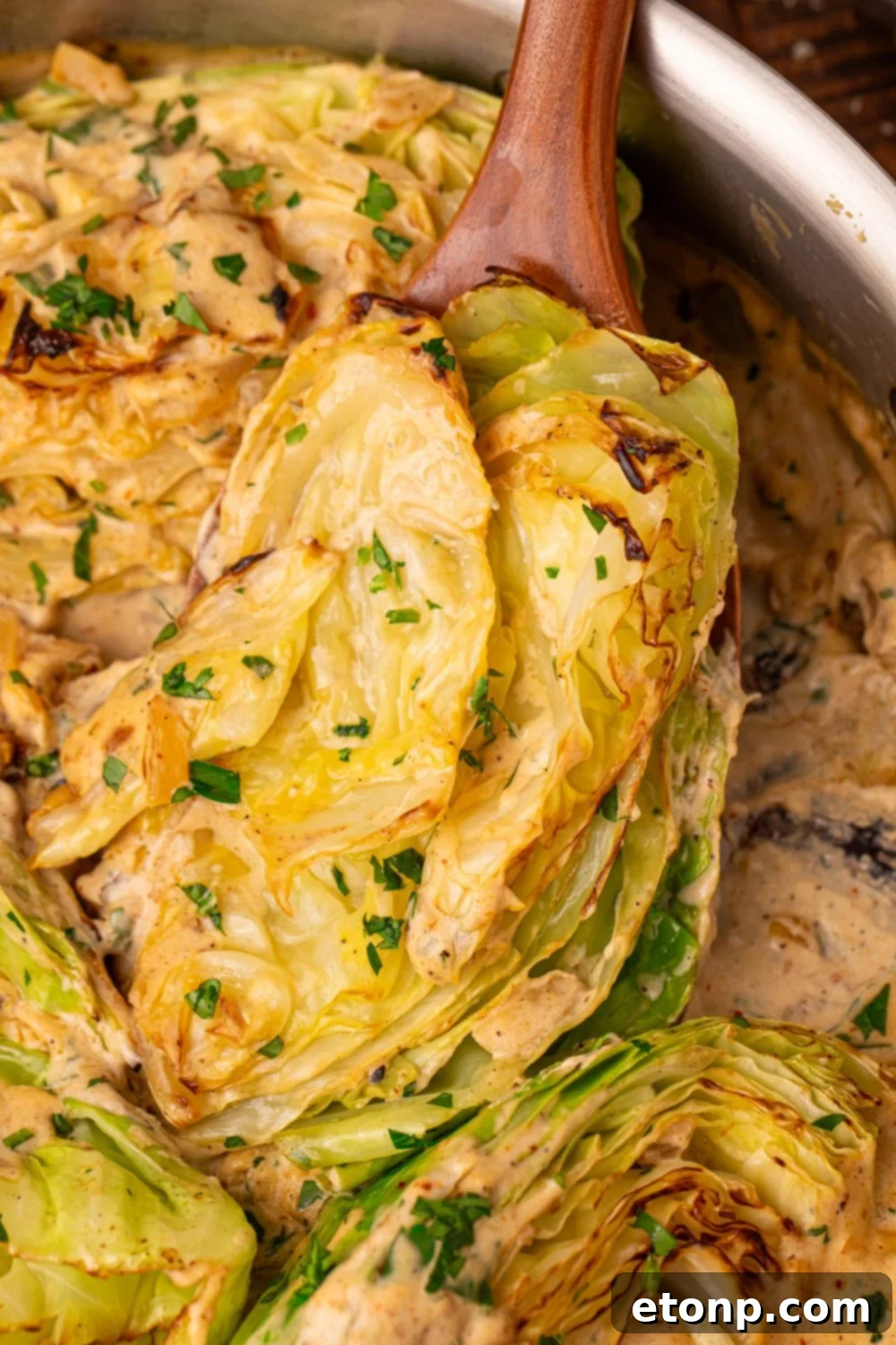Creamy Garlic Parmesan Cabbage in a skillet being lifted out with a wooden spoon 
