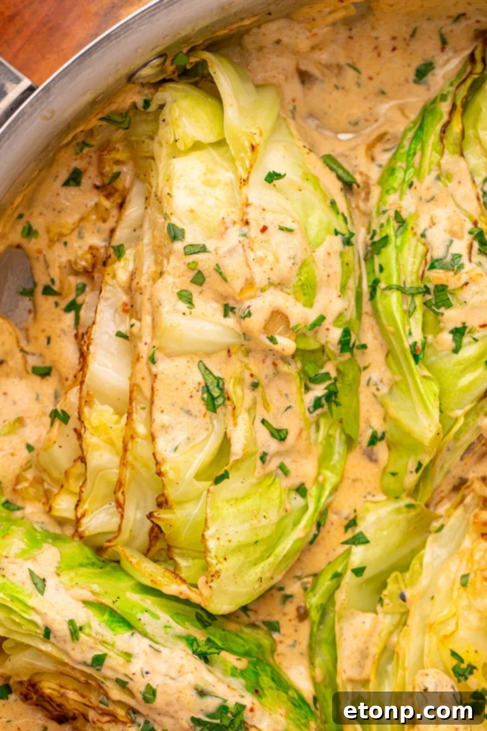 Creamy Garlic Parmesan Cabbage in a skillet on table with some parsley sprinkled over creamy sauce and the cabbage wedges 