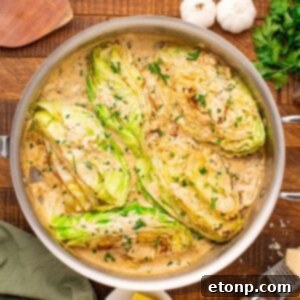 Creamy Garlic Parmesan Cabbage in a skillet on table with parlsey and garlic beside it on table