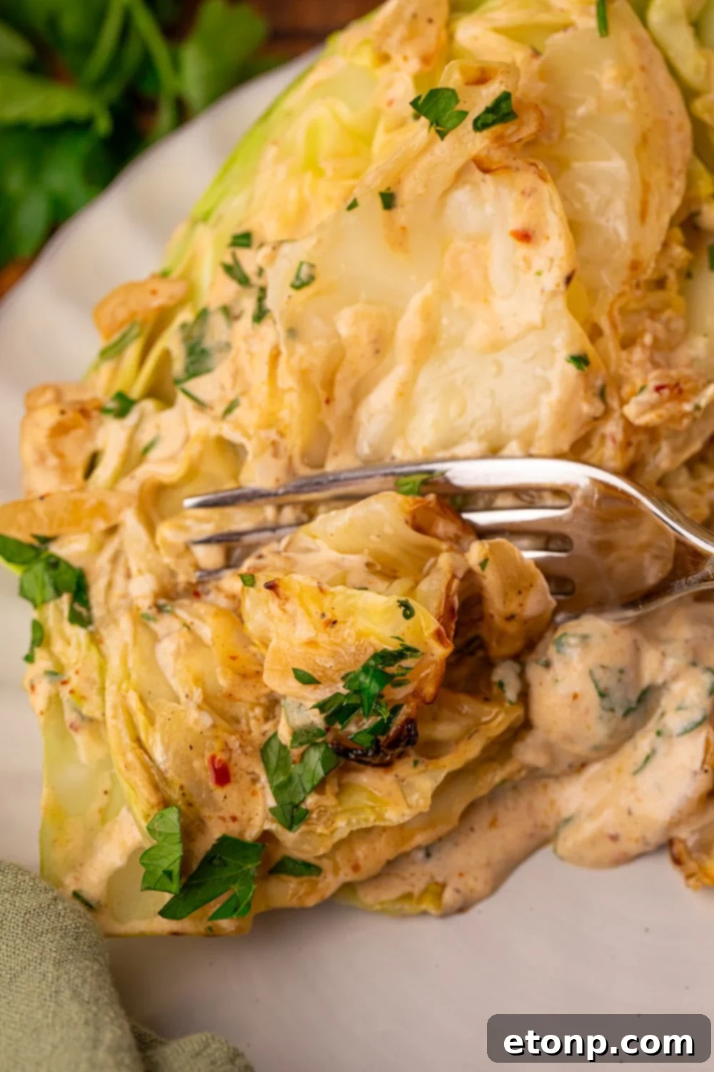 Creamy Garlic Parmesan Cabbage on plate with a fork cutting into a cabbage wedge 