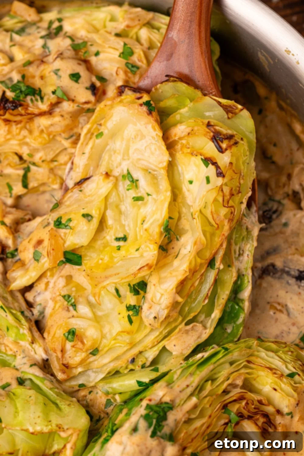 Creamy Garlic Parmesan Cabbage in a skillet with one being lifted out with a spoon 