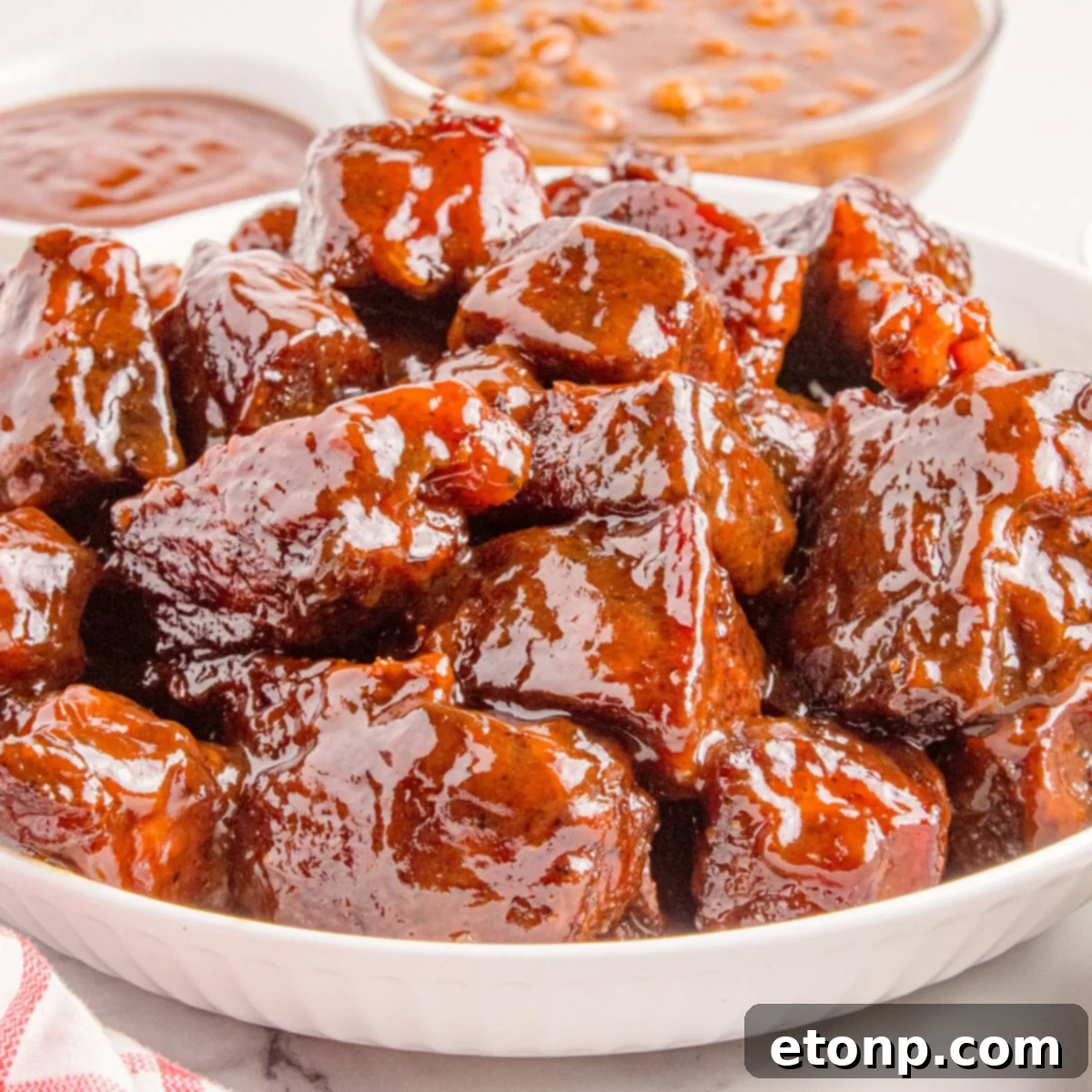 Chuck Roast Burnt Ends in a bowl sitting on table with sauce and beans in background