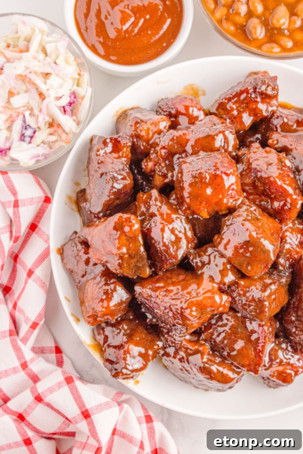 Chuck Roast Burnt Ends on plate with bowls of sauce, coleslaw, and beans