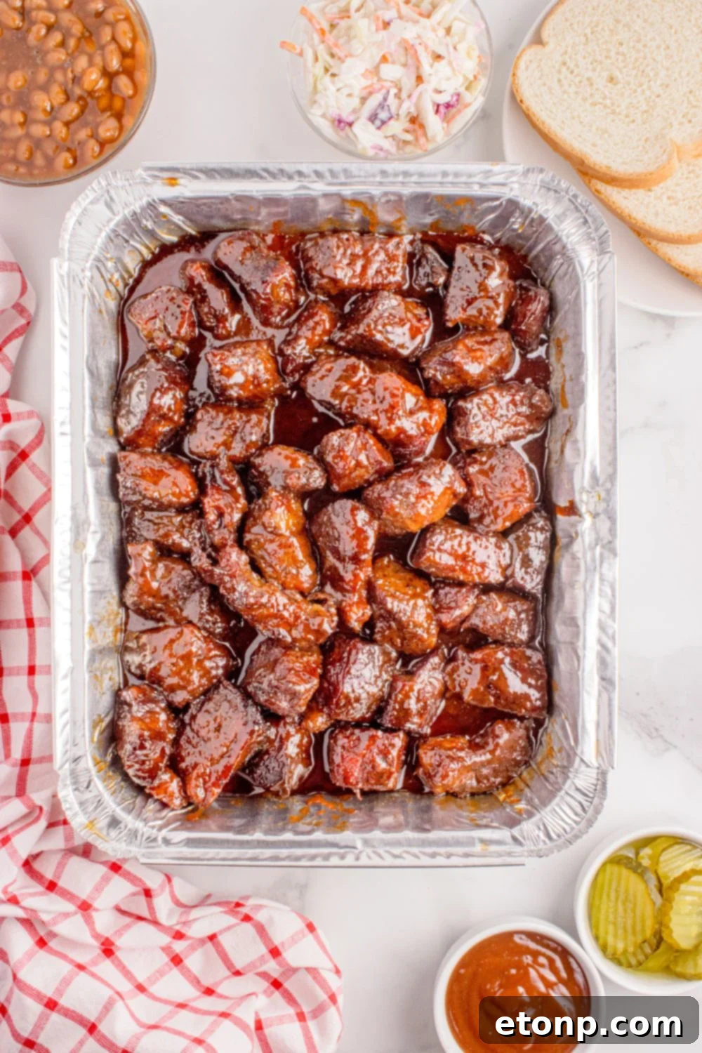 Chuck Roast Burnt Ends in a tin foil pan with bread, coleslaw, pickles, and more all around the pan