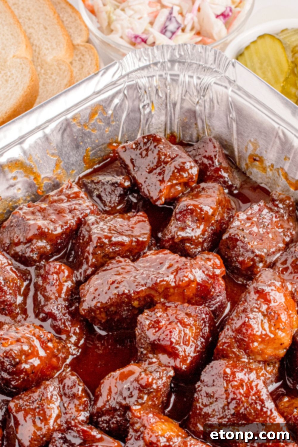 Chuck Roast Burnt Ends in a pan on table with sliced bread to the side and a small bowl of pickles