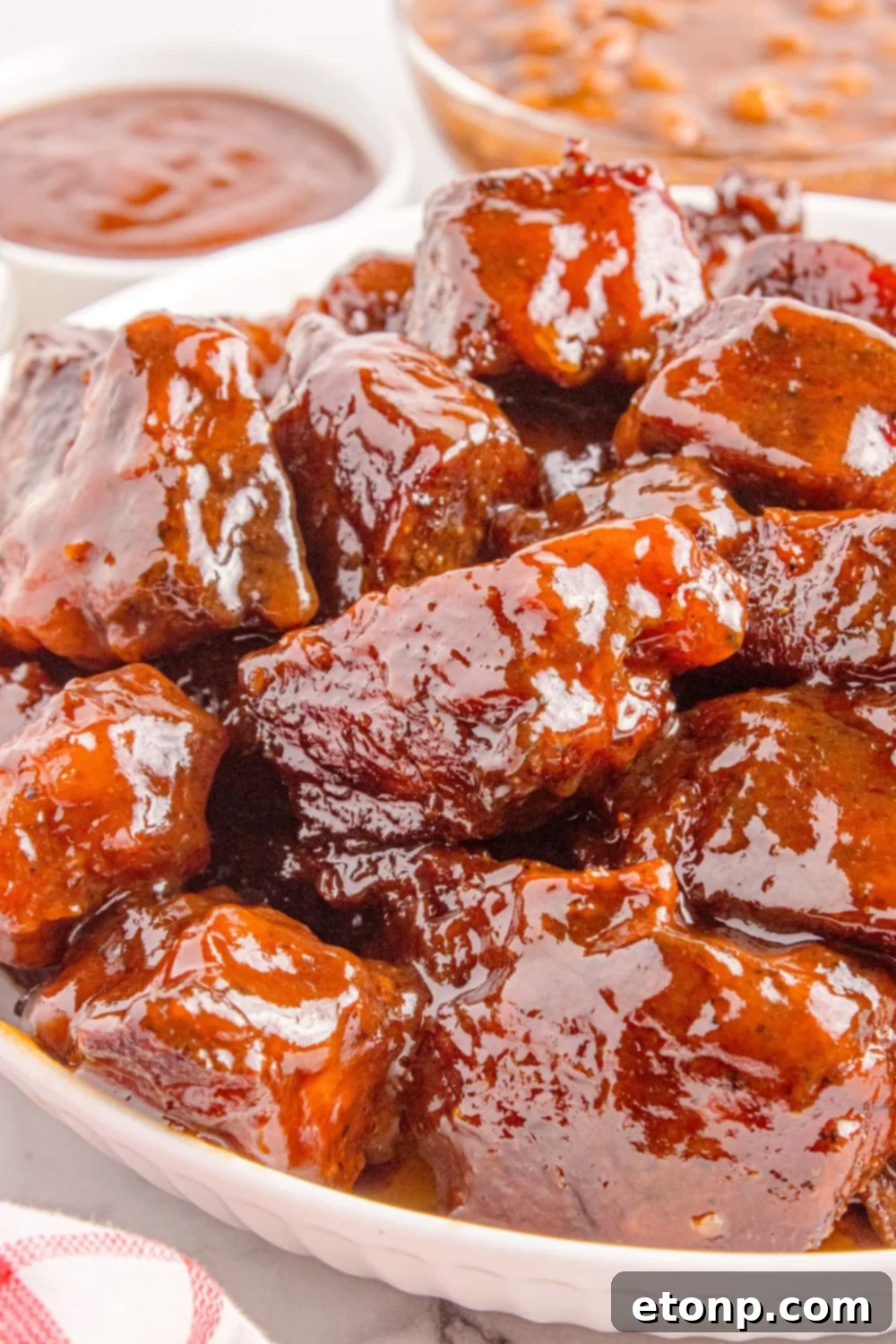Chuck Roast Burnt Ends piled in a white bowl sitting on table with a small bowl of bbq sauce to side