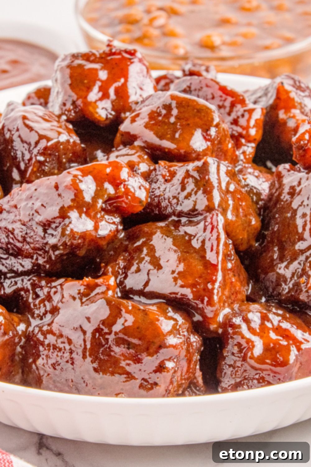 Chuck Roast Burnt Ends in a white bowl on a table with a bowl of beans to the side