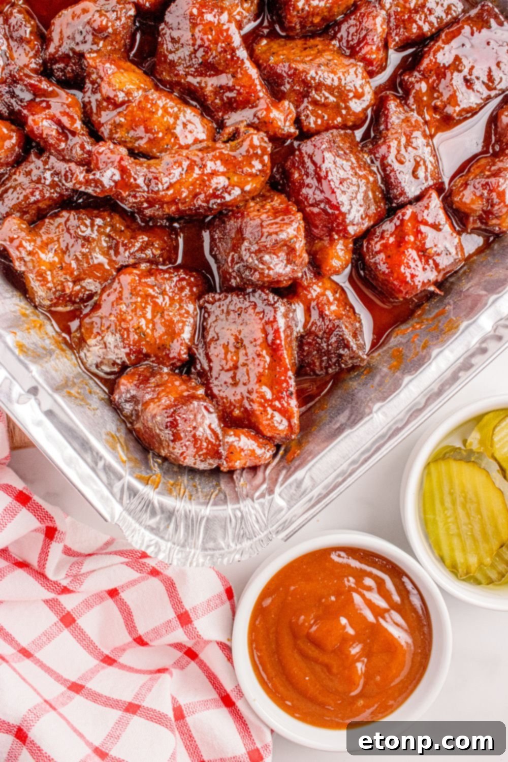 Chuck Roast Burnt Ends in a foil tray with sauces and pickles to side of container