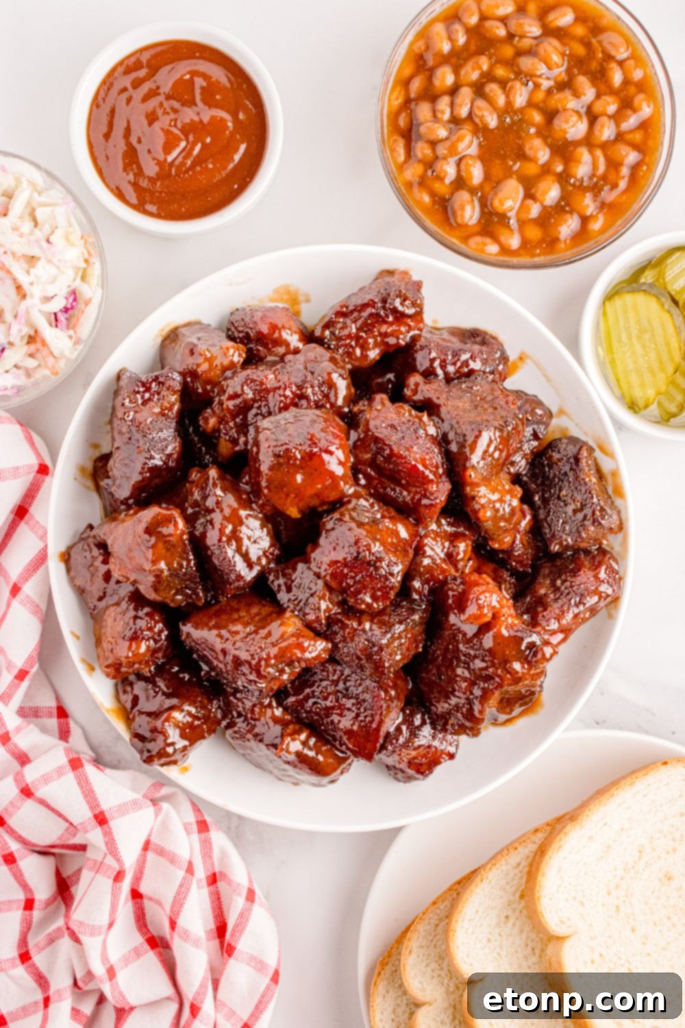 Chuck Roast Burnt Ends in a bowl with a bowl of beans on side, pickles, and sauce around the meat