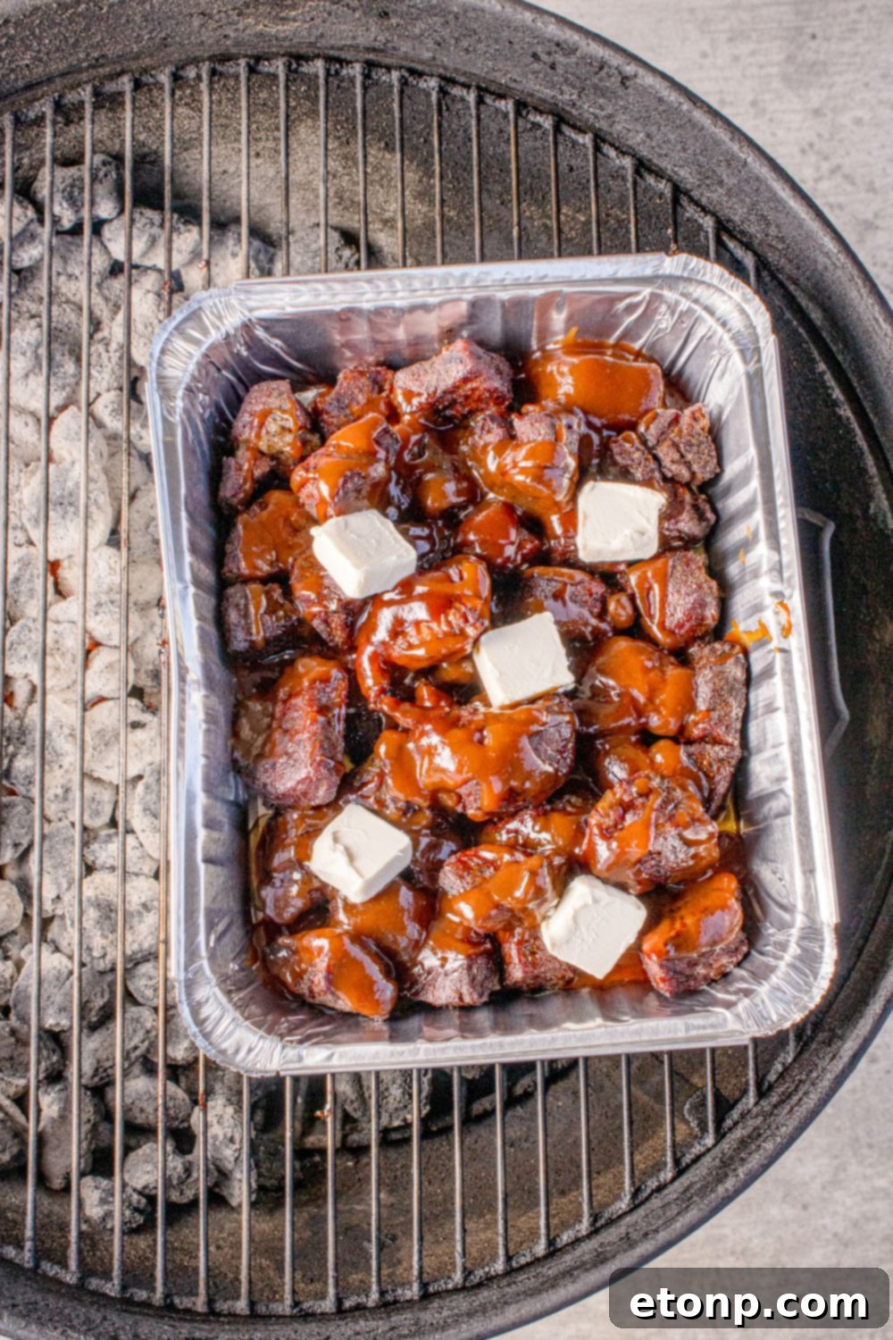 Chuck Roast Burnt Ends in a pan on charcoal grill with butter on top