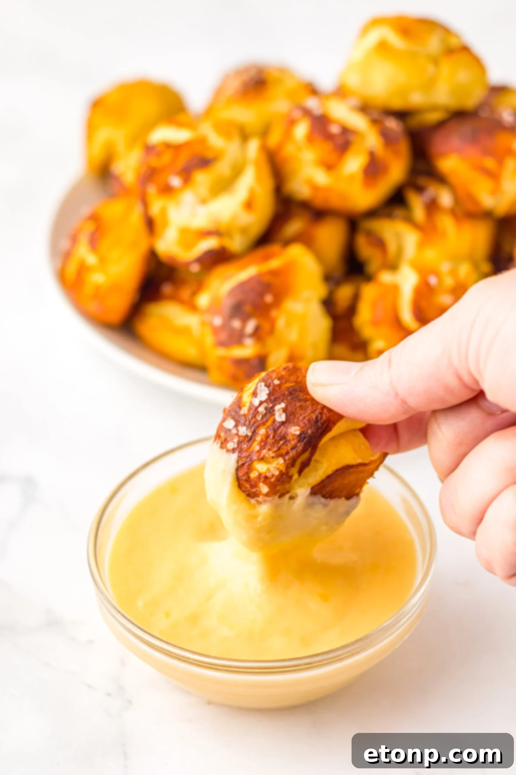 Easy Biscuit Pretzel Bites with a hand dipping one into the Cheese Sauce