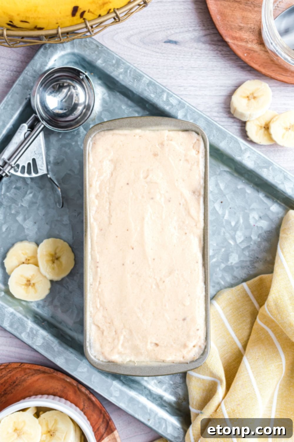 Effortless One-Ingredient Banana Ice Cream 13 Banana Ice Cream in a loaf pan with fresh bananas sliced to side and an ice cream scoop to side of pan