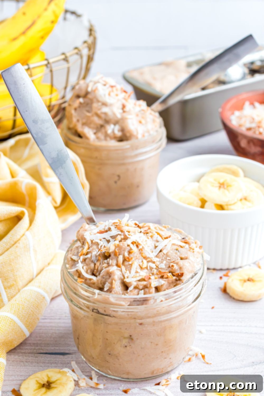 Effortless One-Ingredient Banana Ice Cream 15 Banana Ice Cream in bowls with toppings on top and spoons in bowls, and bananas sliced in a white bowl on table