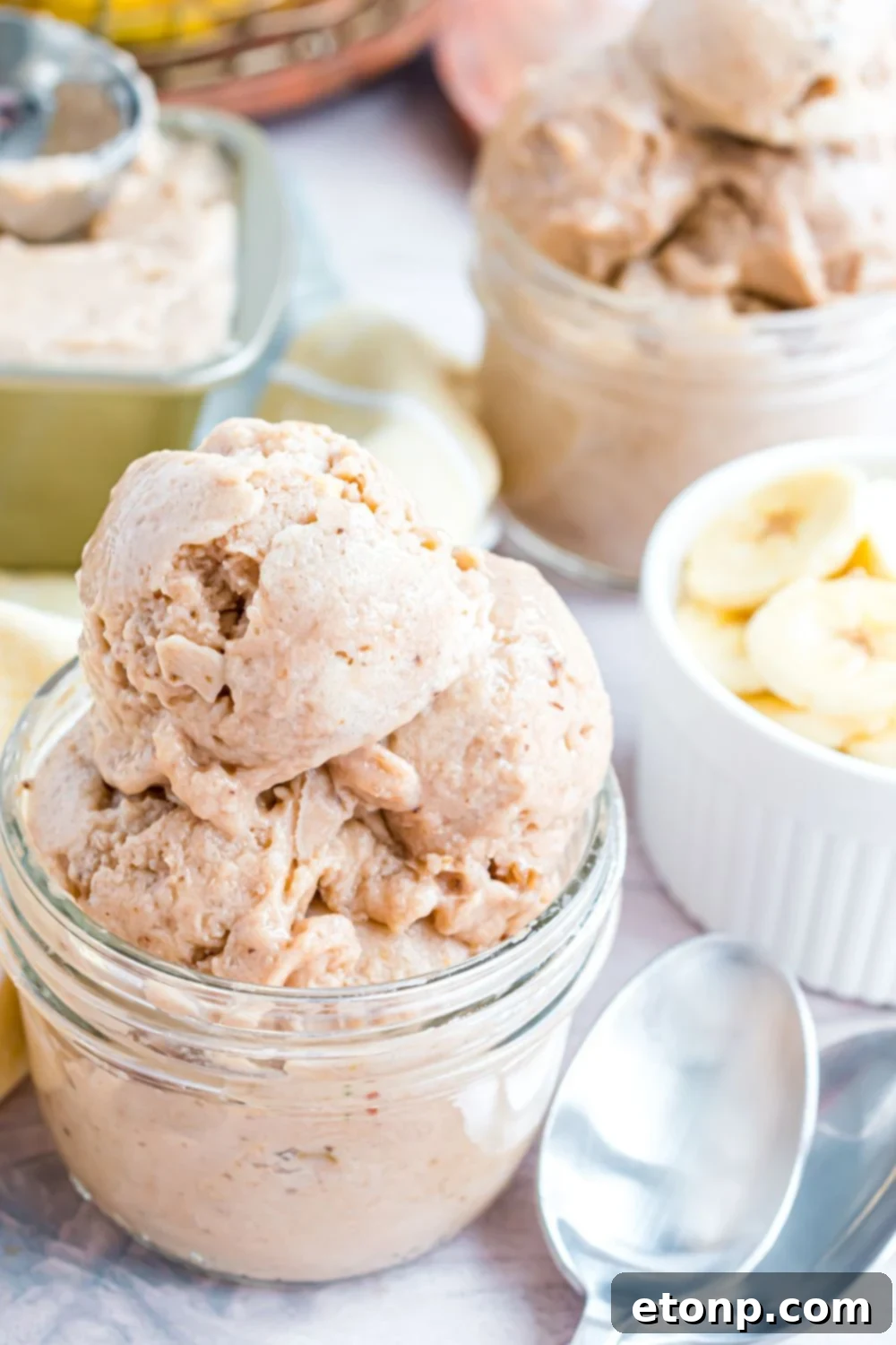 Effortless One-Ingredient Banana Ice Cream 18 Banana Ice Cream in a glass bowl with fresh sliced bananas to side and spoons on table