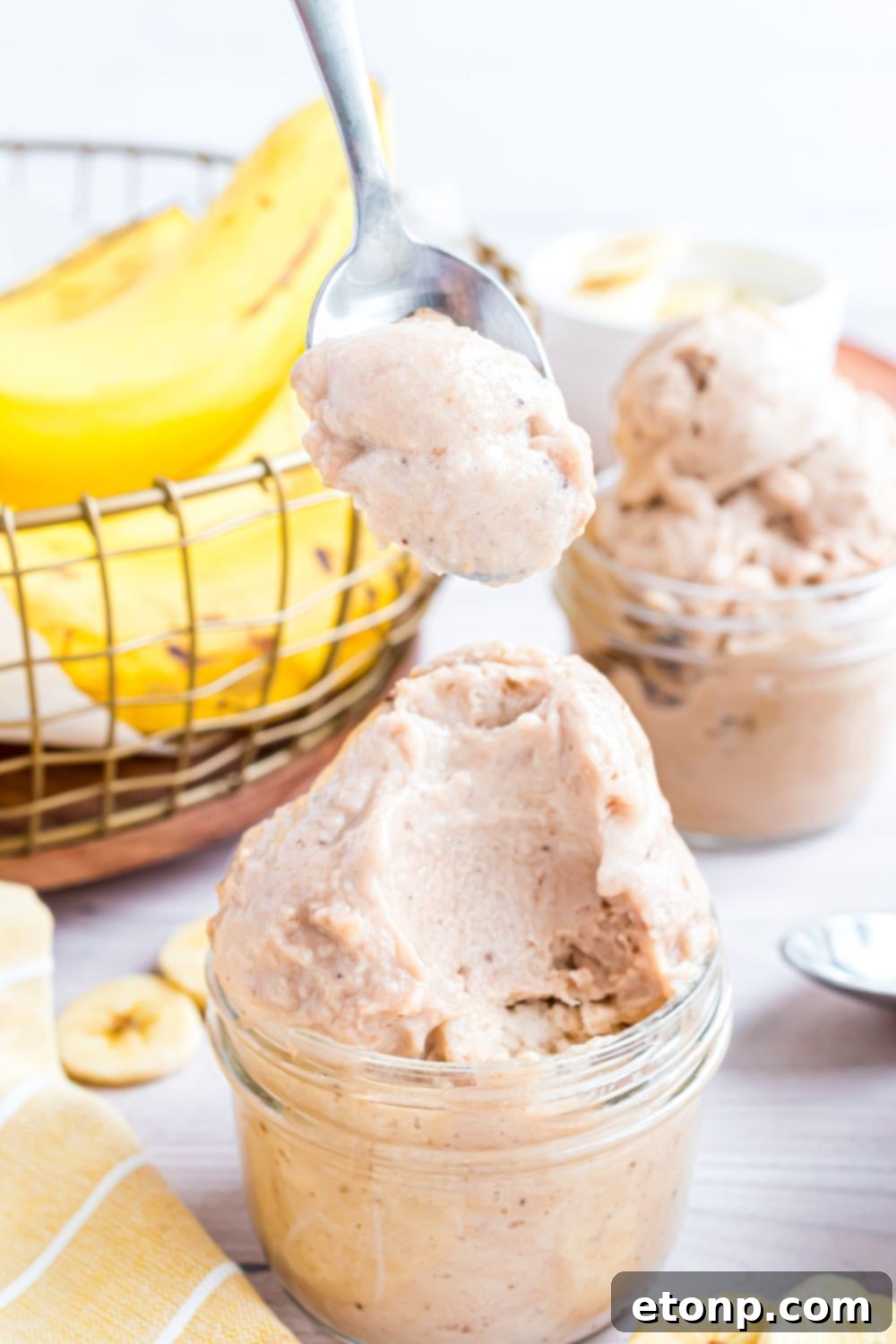 Effortless One-Ingredient Banana Ice Cream 21 Banana Ice Cream in jars on table with sliced banana to side and a bowl of bananas behind it on table