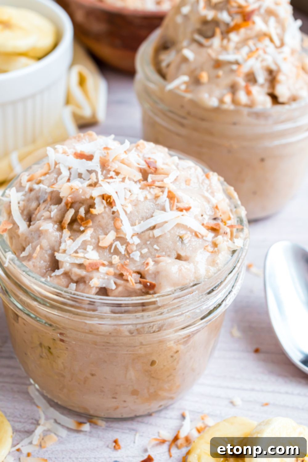 Effortless One-Ingredient Banana Ice Cream 22 Banana Ice Cream in bowl topped with toasted coconut, and spoons and nuts around table