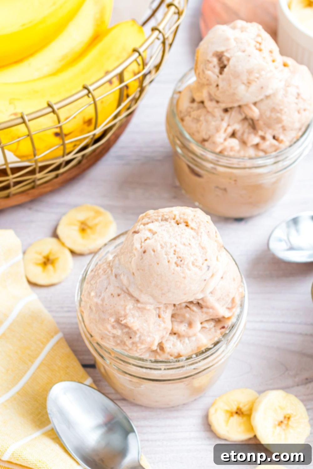 Effortless One-Ingredient Banana Ice Cream 23 Banana Ice Cream in small bowls on table with a bundle of bananas to side and sliced bananas on table