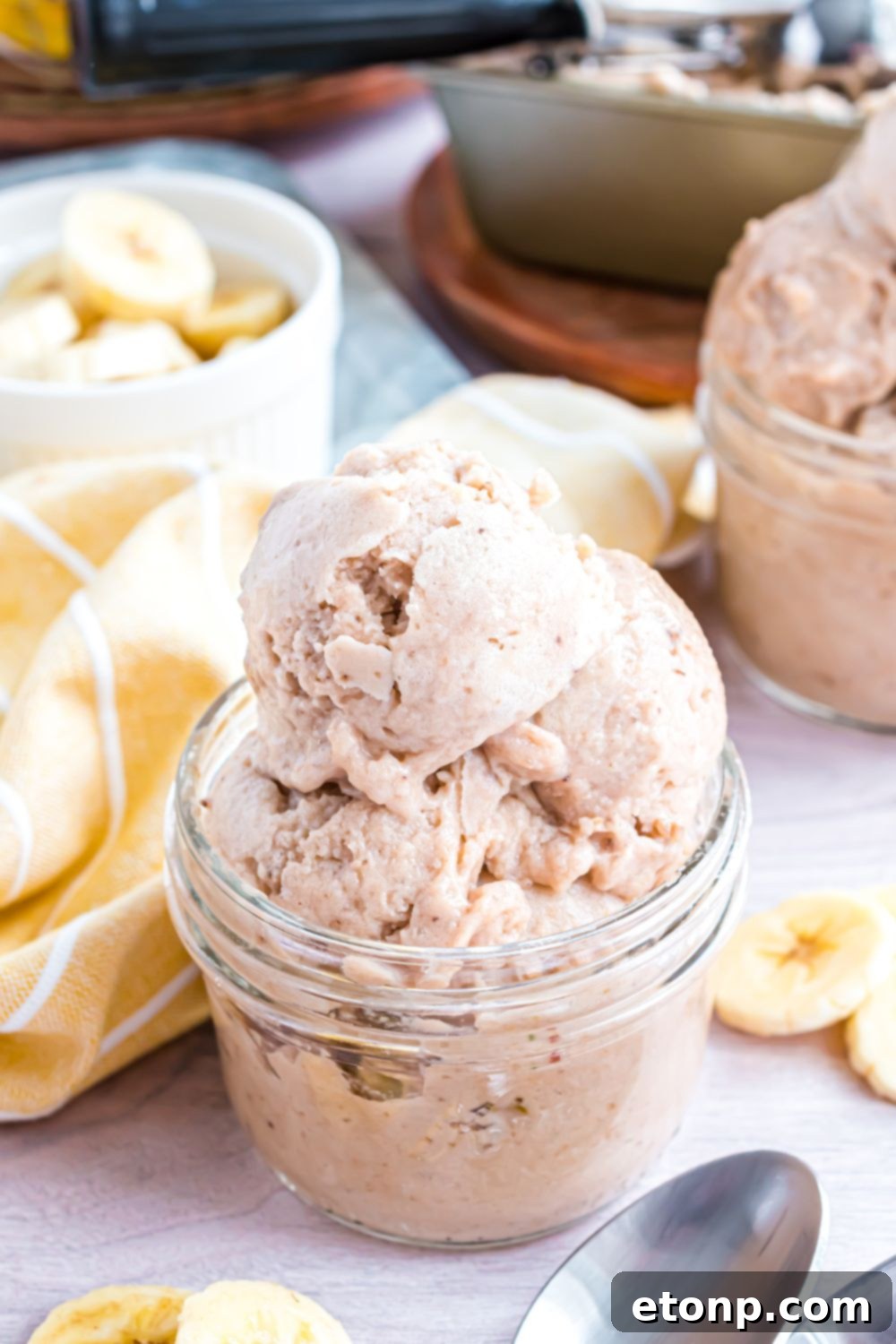 Effortless One-Ingredient Banana Ice Cream 24 Banana Ice Cream in jars with a yellow towel between bowls and sliced bananas in a bowl behind the ice cream