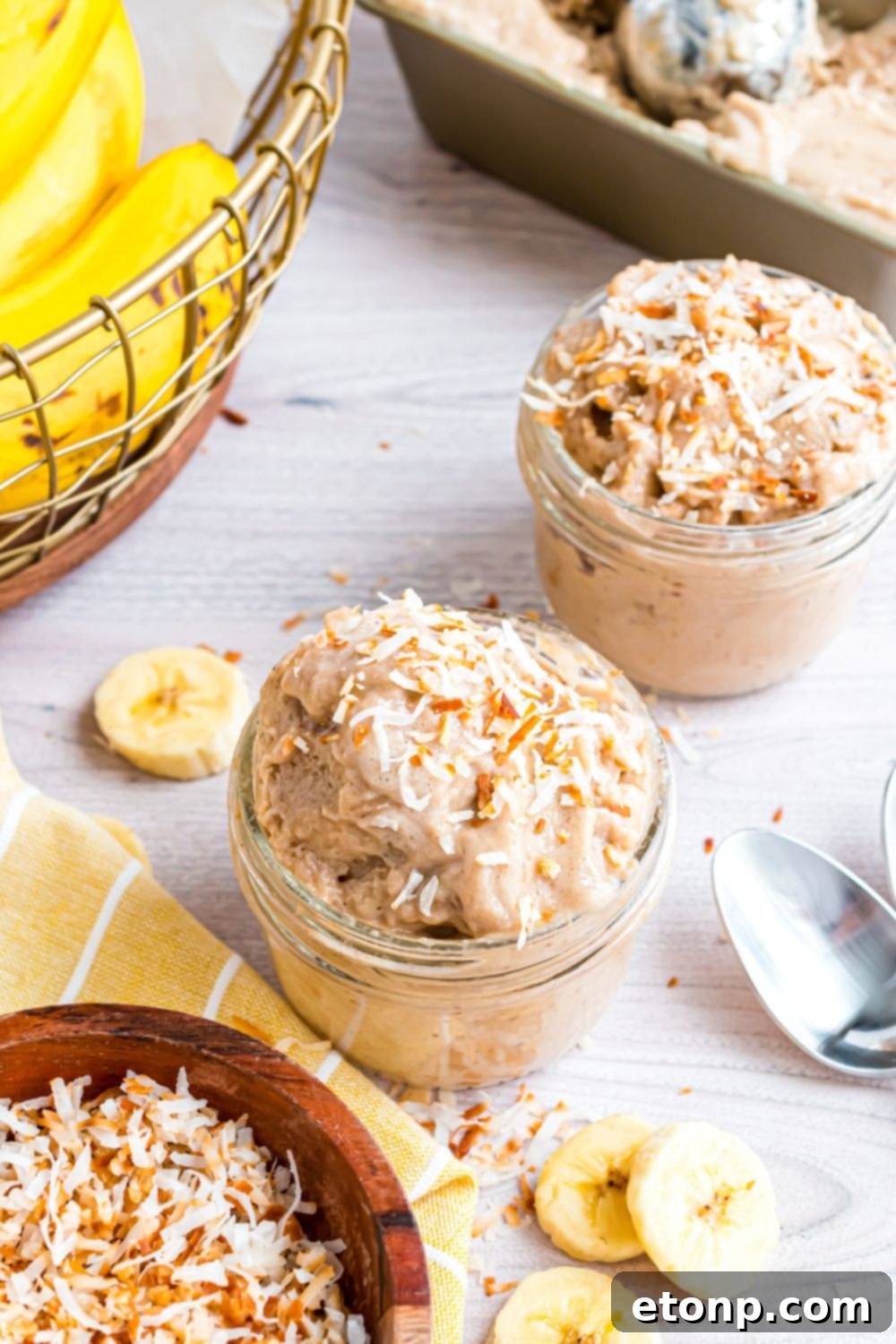 Effortless One-Ingredient Banana Ice Cream 4 Banana Ice Cream in glass bowls on table with a basket of bananas to side, and spoons and sliced bananas on table