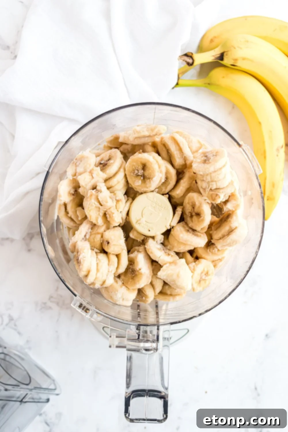 Effortless One-Ingredient Banana Ice Cream 8 frozen bananas in a food processor with bananas to side for making Banana Ice Cream