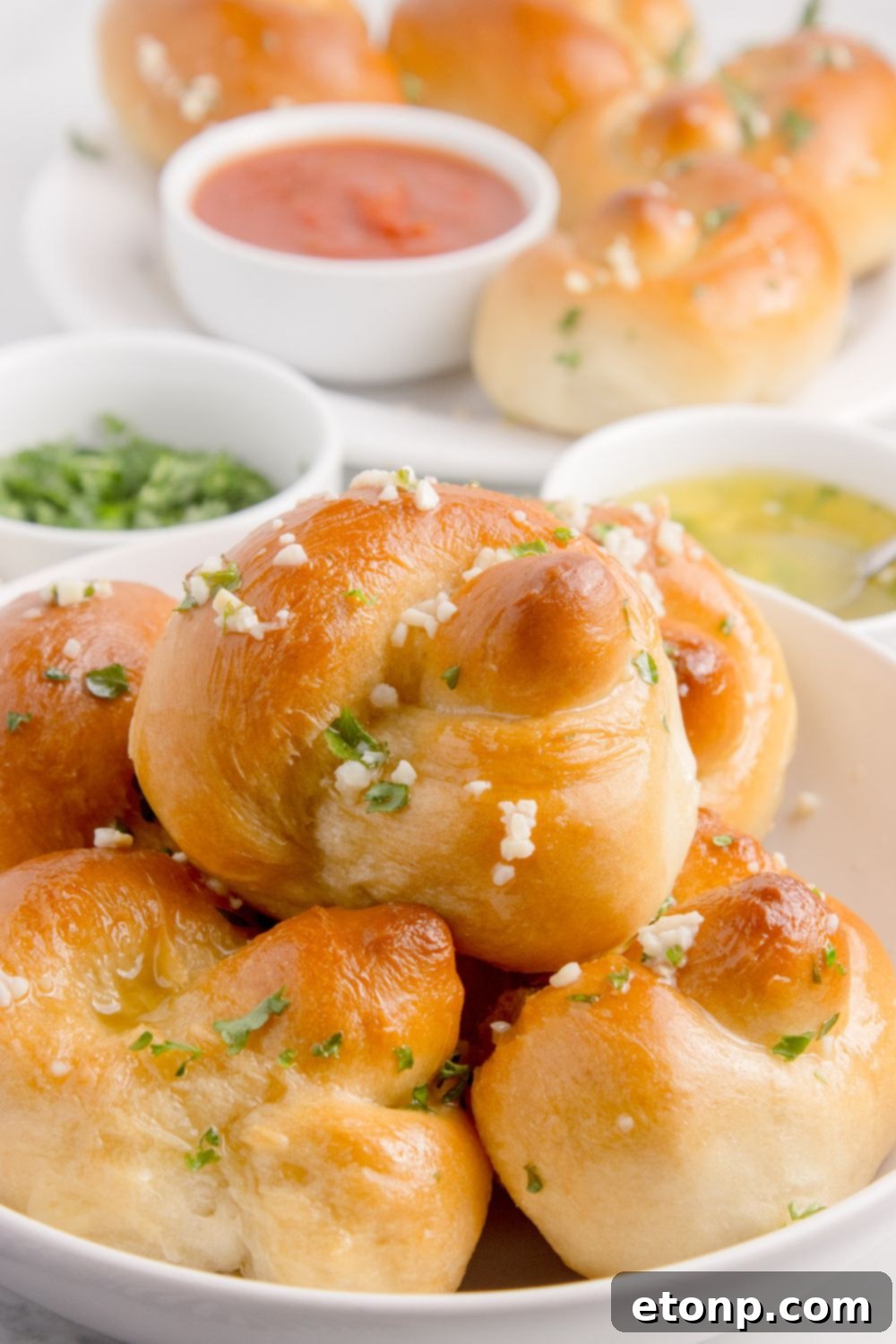 Homemade Garlic Knots in a bowl with garlic butter in a bowl, parsley and a bowl of marinara sauce 
