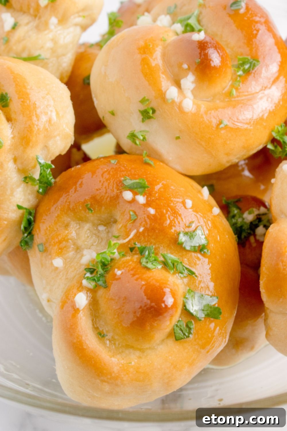 Homemade Garlic Knots on a table topped with garlic and parsley and melted butter 