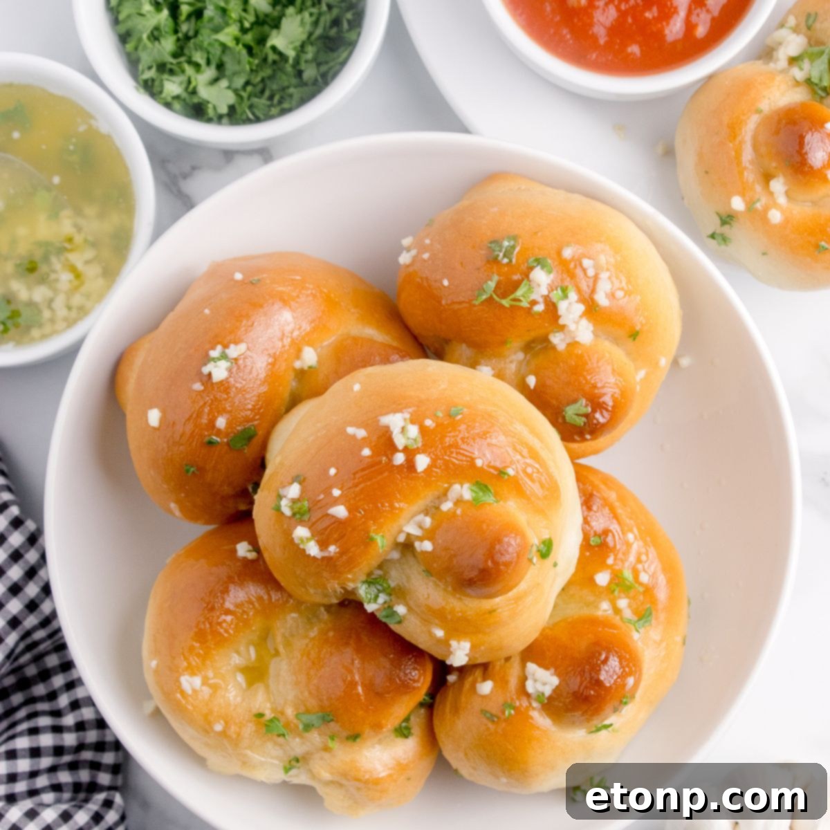 Homemade Garlic Knots piled out on a plate with butter, parsley and dipping sauces to side