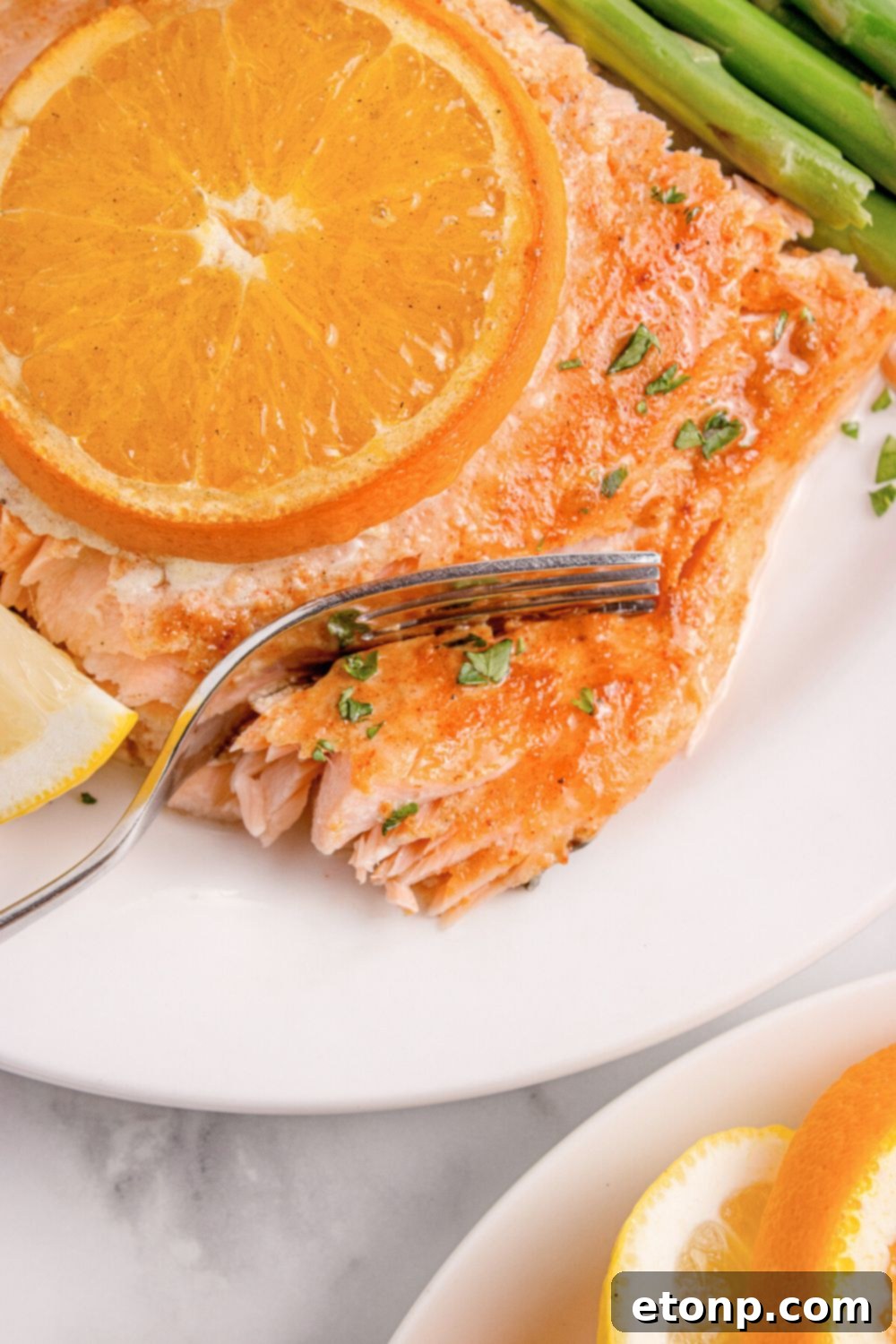Simple Grilled Honey Mustard Salmon Foil Packets 16 salmon on plate with an orange on top, with a fork cutting into the salmon, and asparagus to side