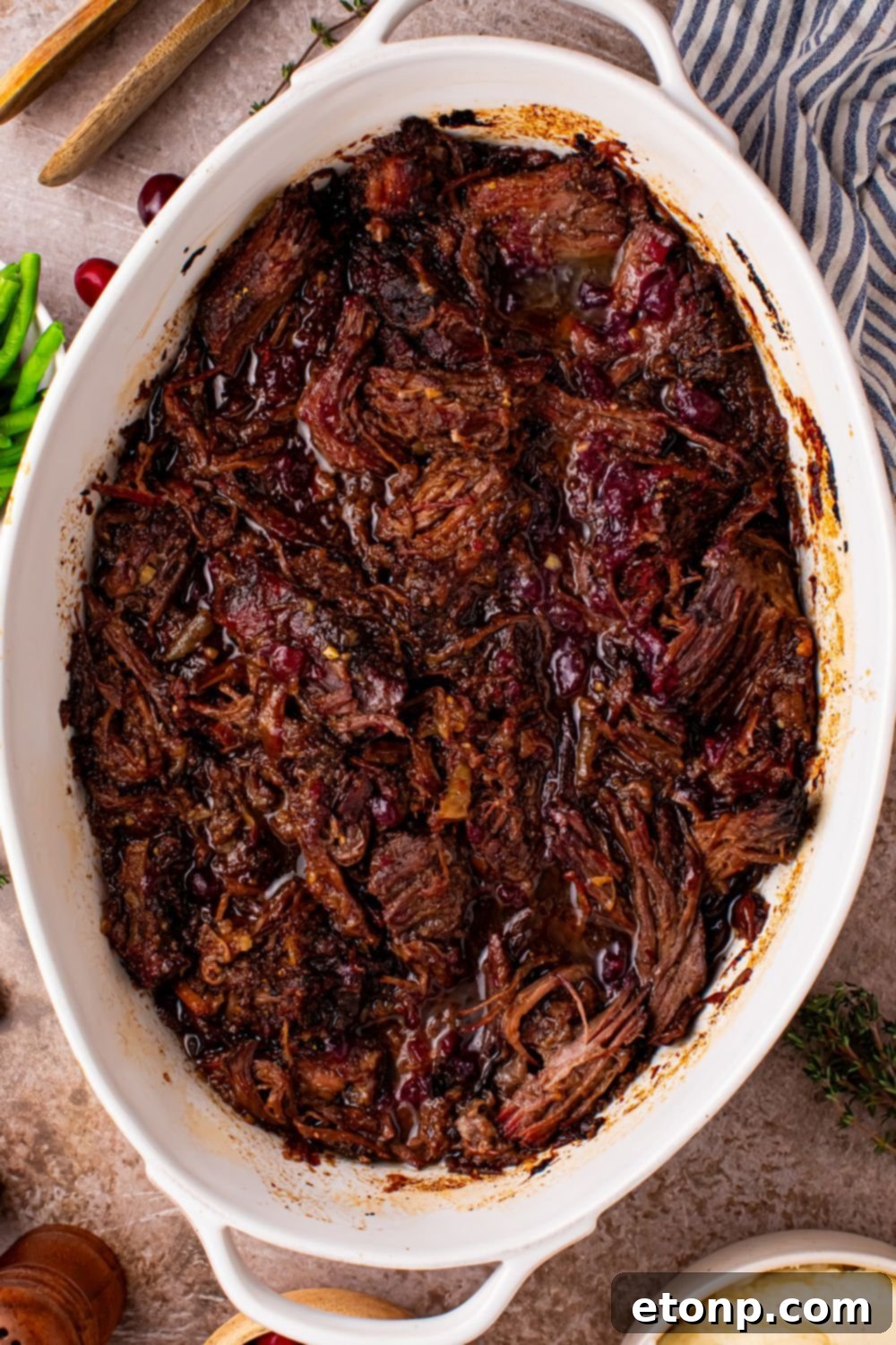 Cranberry Pot Roast shredded and in a pan on table with a towel to side of pan 