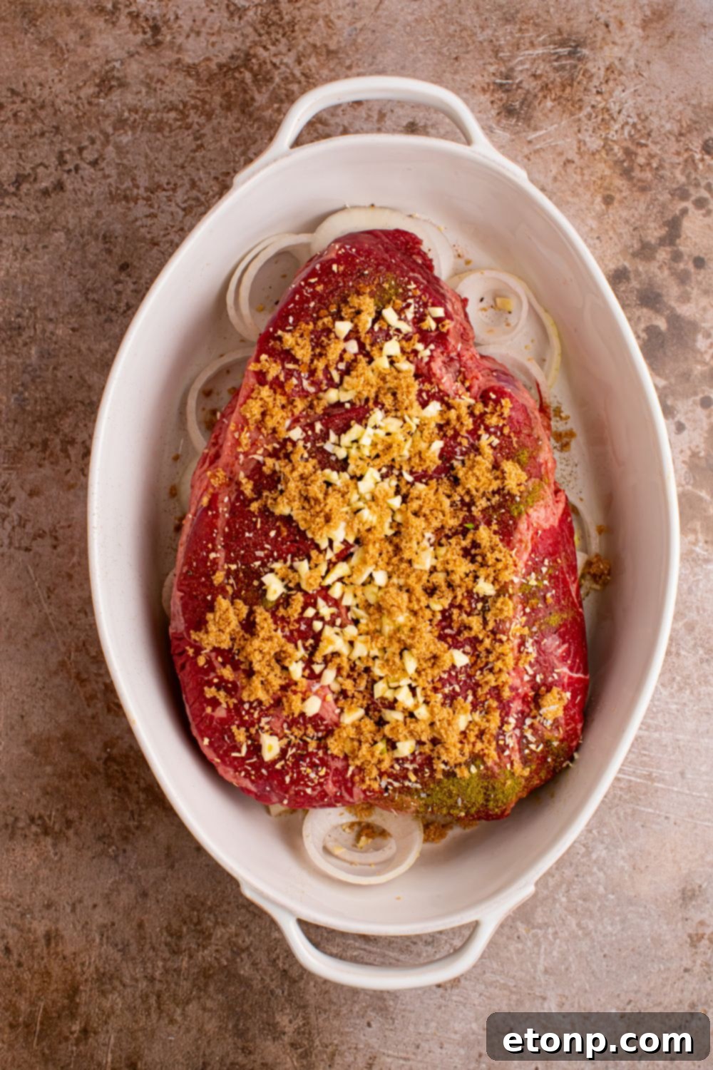 casserole dish with onions and pot roast on top with spices and seasonings 